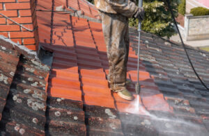 a professional pressure washing the clay tiles on the roof of a home